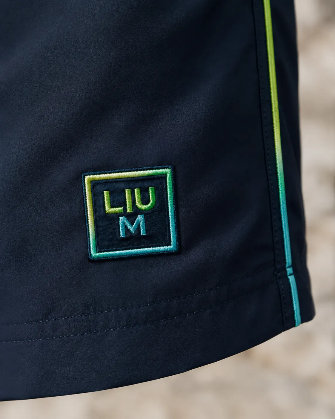 Close-up of the embroidered LIUM patch on navy swim shorts