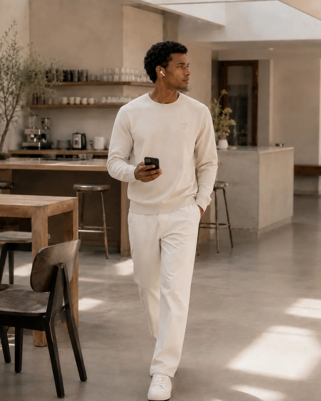 A man in a cream LIUM sweater walks through a bright café