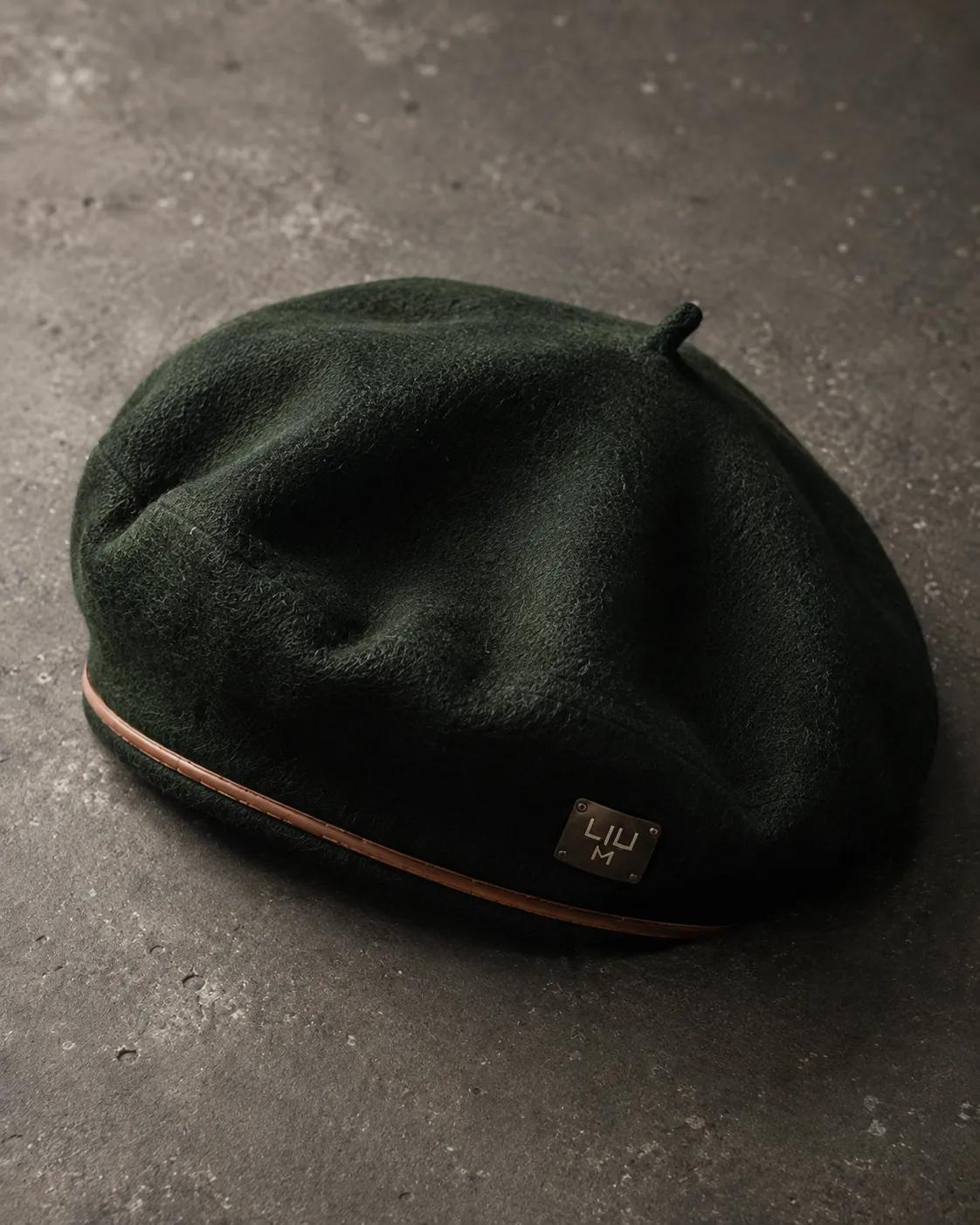 A dark green LIUM beret with a copper stripe on dark stone